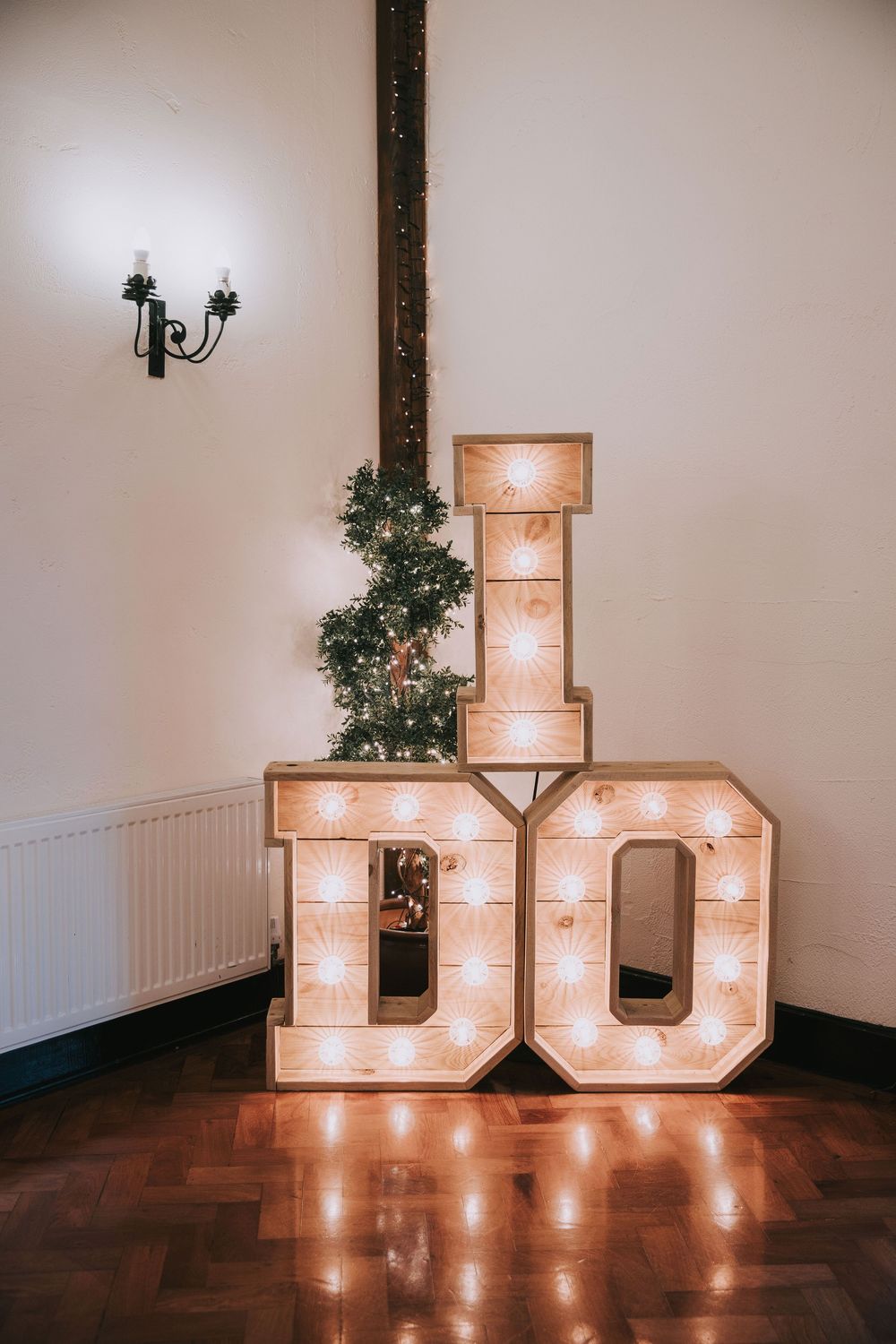 Illuminated marquee letters spelling 'I DO' decorated with greenery create a romantic wedding venue display on dark hardwood floors.