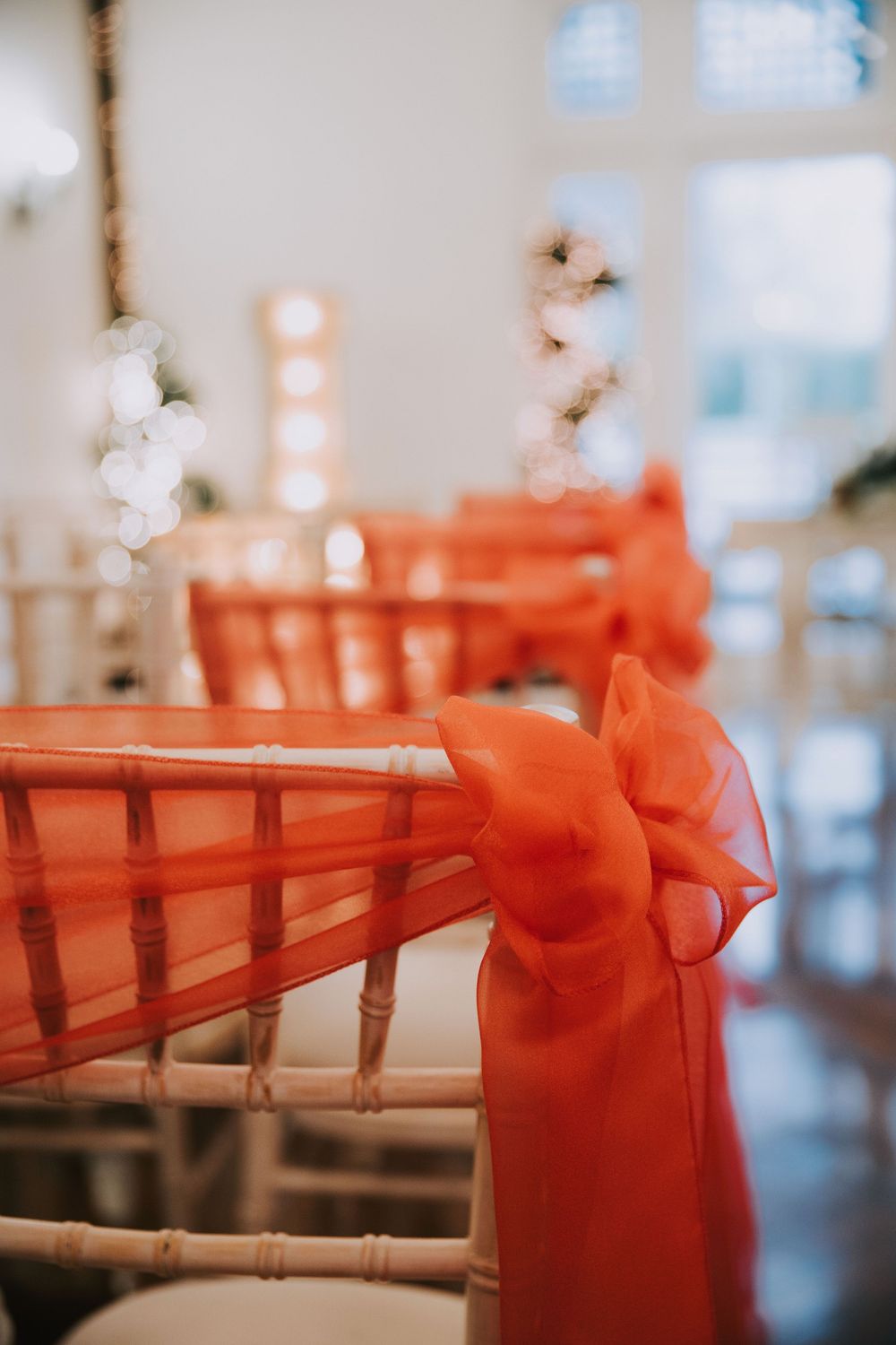 An orange chiffon bow decorates a wooden chiavari chair at an elegant event venue.