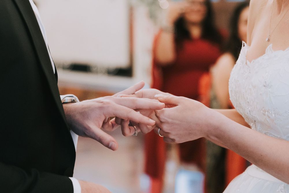 Close-up view of hands exchanging wedding rings during a marriage ceremony.