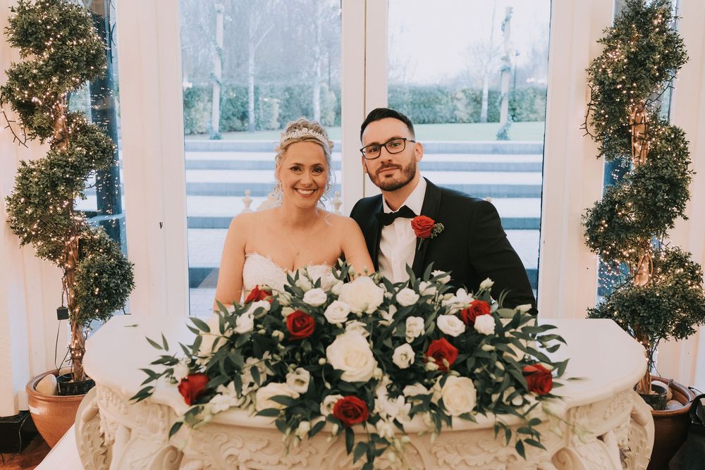 A wedding reception venue decorated with elegant greenery garlands and white floral arrangements along a bright windowed wall.