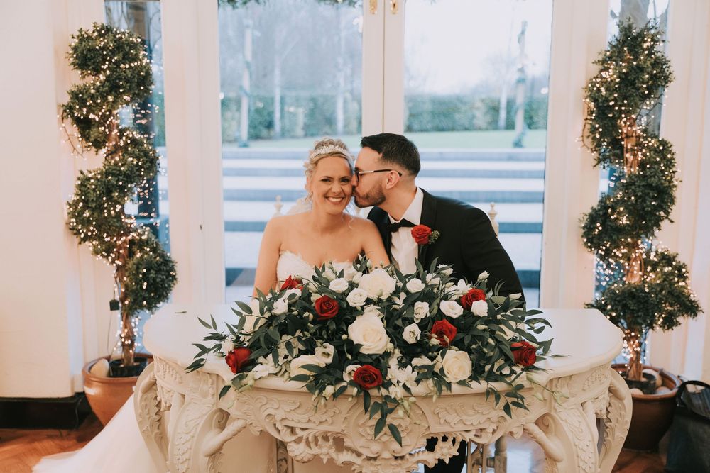 Elegant wedding reception setup with white floral arrangements and greenery decorating a light-filled venue space.
