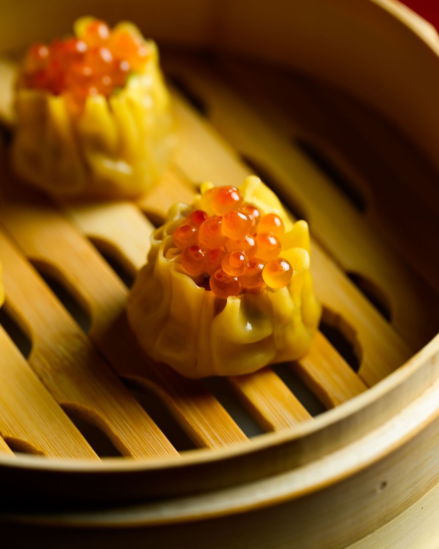 Steamed dumplings topped with bright orange roe served in a traditional bamboo steamer basket.