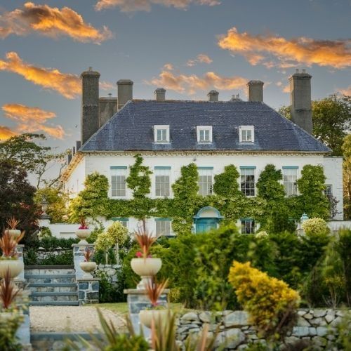 Row of traditional stone cottages with gardens at sunset under golden clouds.