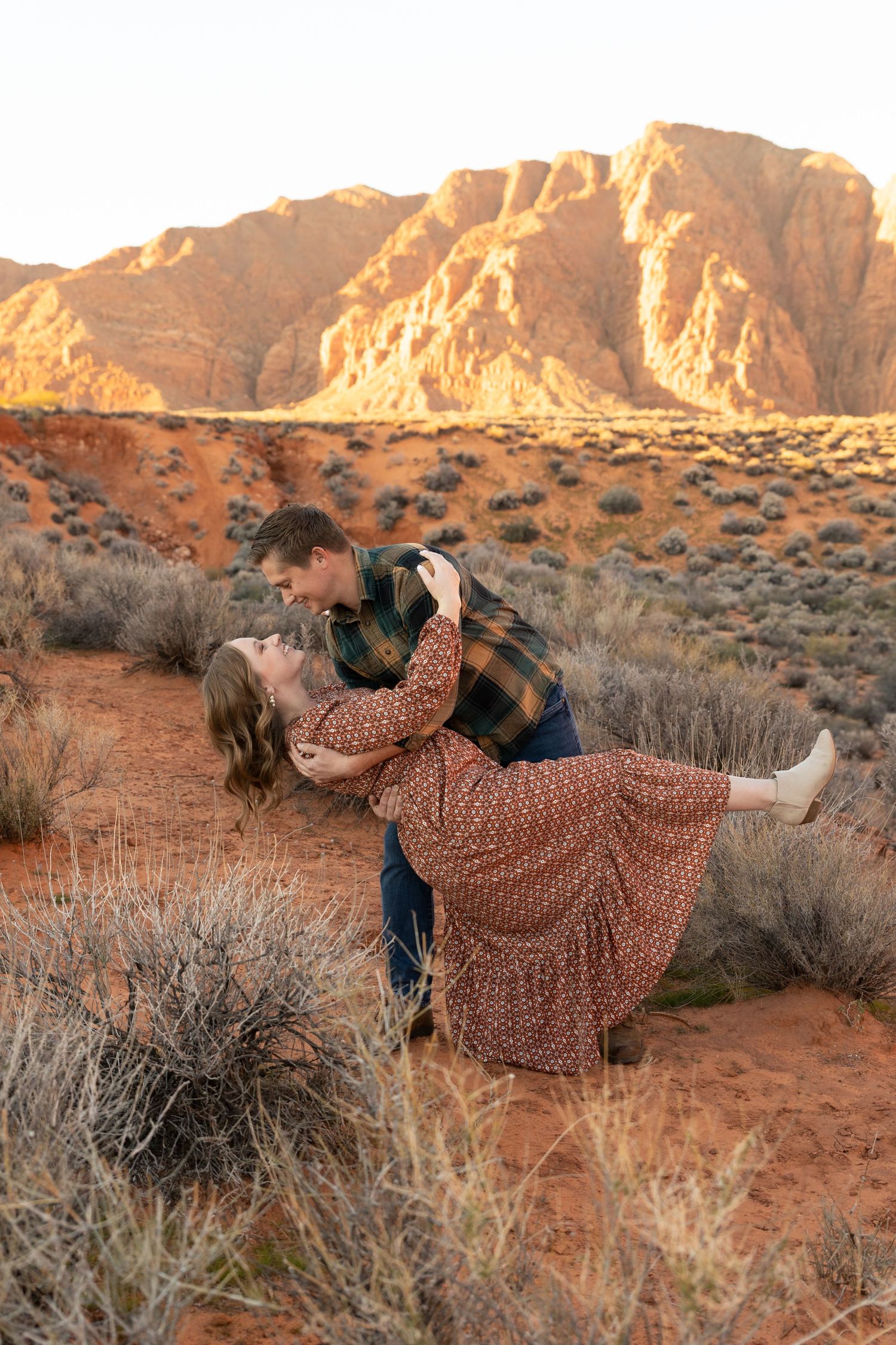 man dipping woman in a pretty brown long dress. she is kicking her leg out and smiling at him