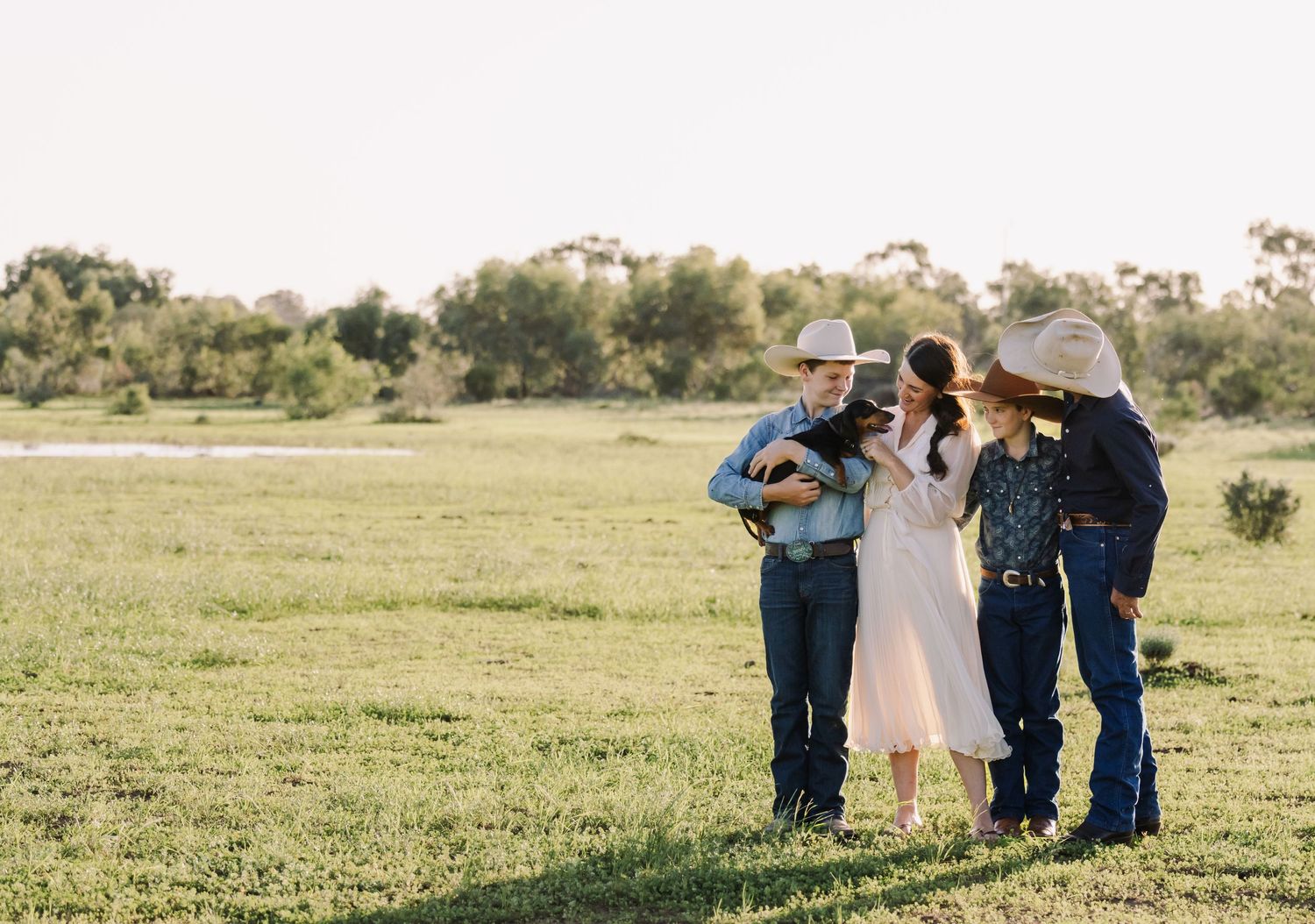 Group gathered in casual western attire on grassy field with trees in background.