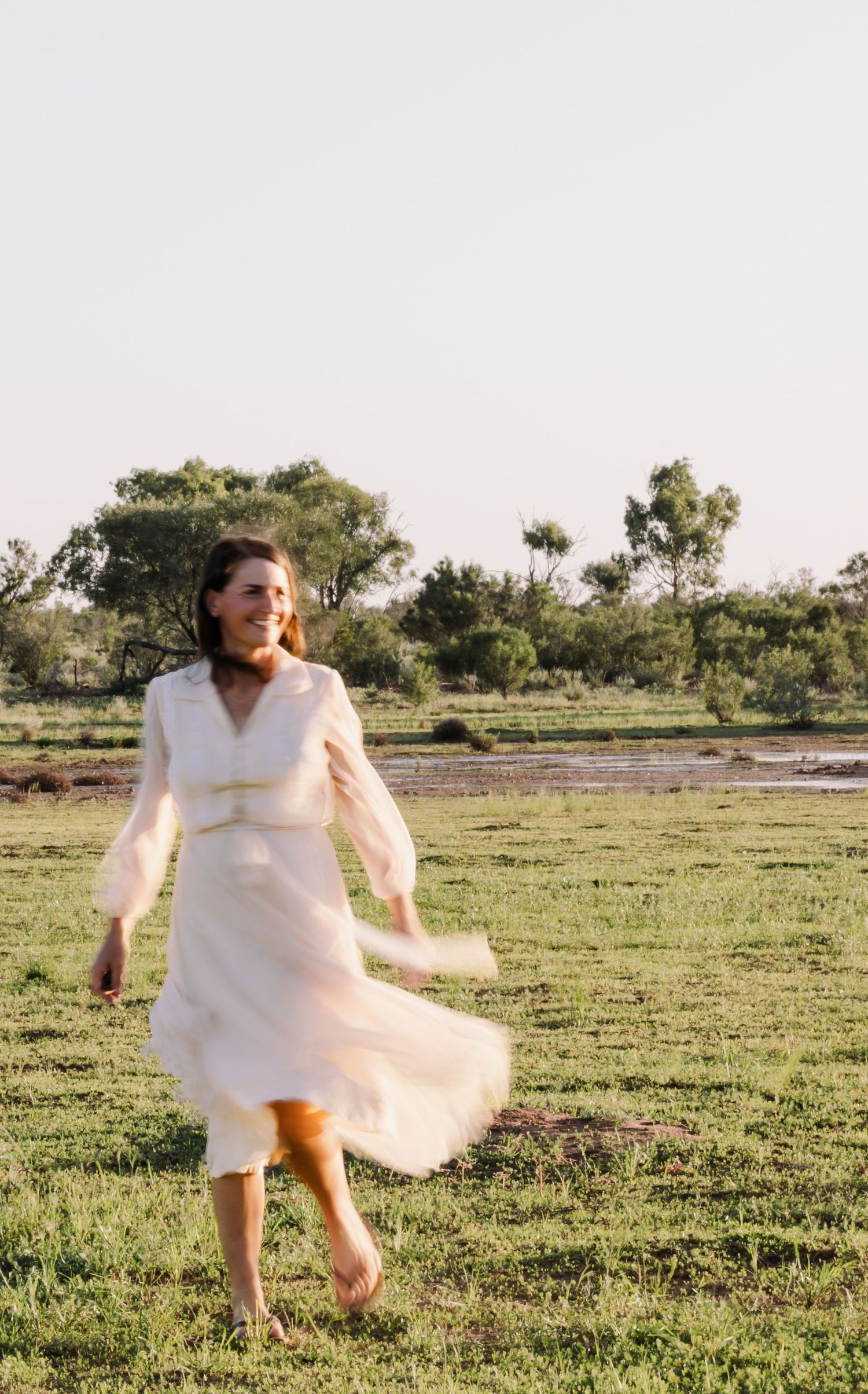 Woman in flowing white dress dancing in rustic outdoor setting.