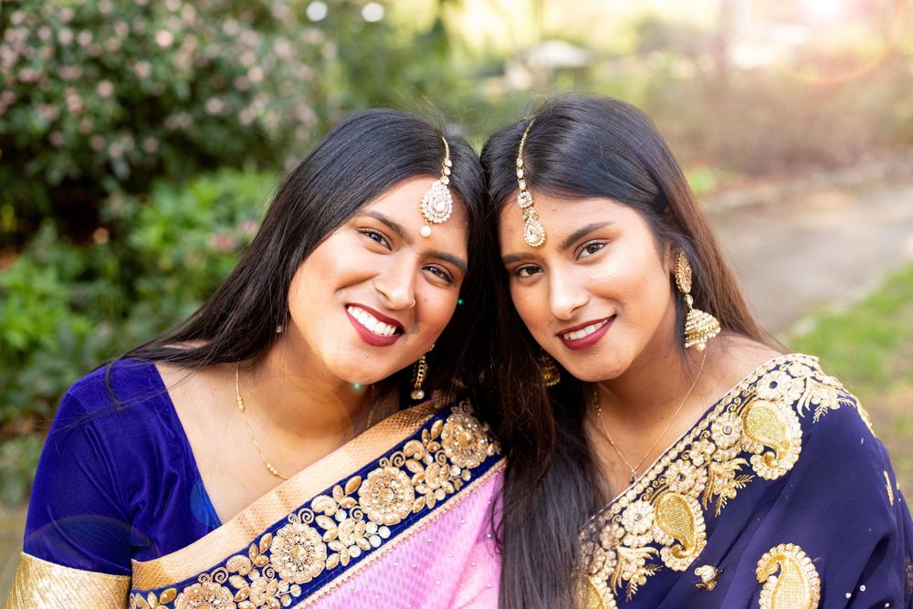 Two women in traditional navy blue and gold saris smile together outdoors in natural lighting.
