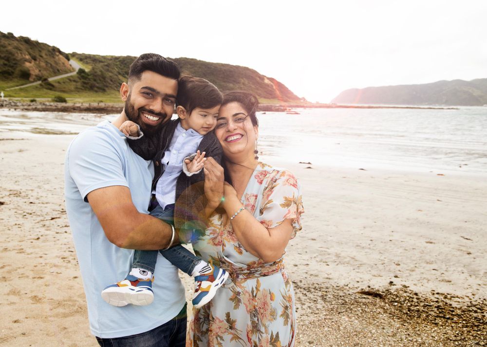A family enjoys a sunny moment together on a scenic beach with coastal cliffs in the background.
