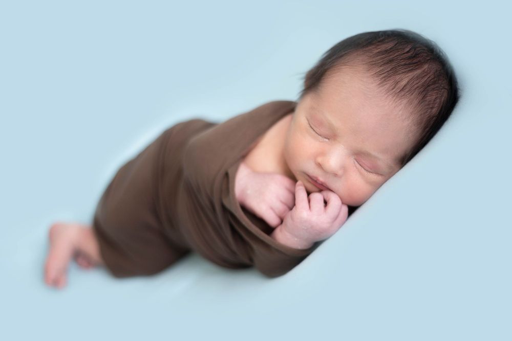 Peaceful sleeping newborn baby wrapped in brown cloth against light blue background.