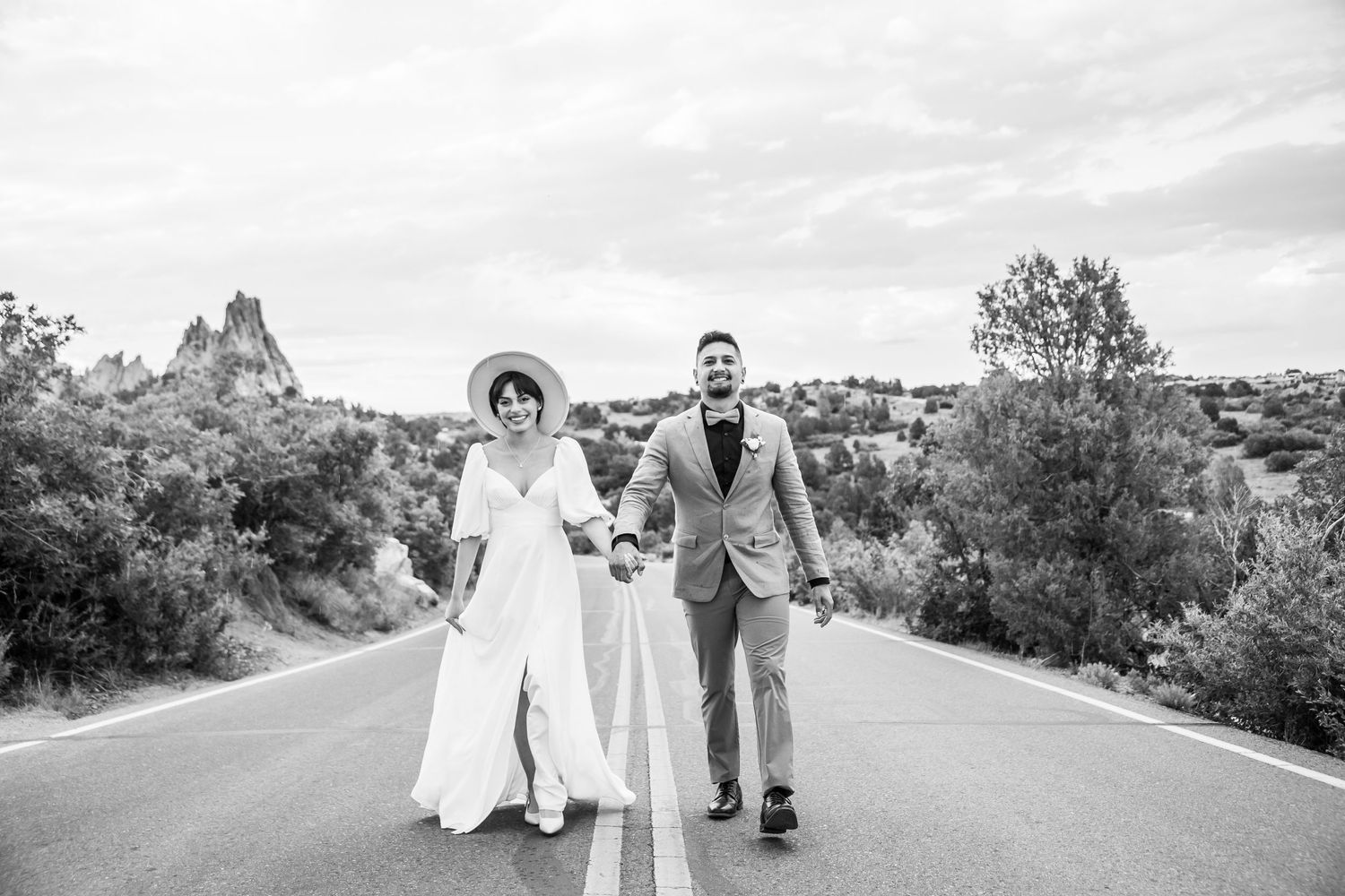 A couple in wedding attire walks down the center of an empty rural road together on their special day.