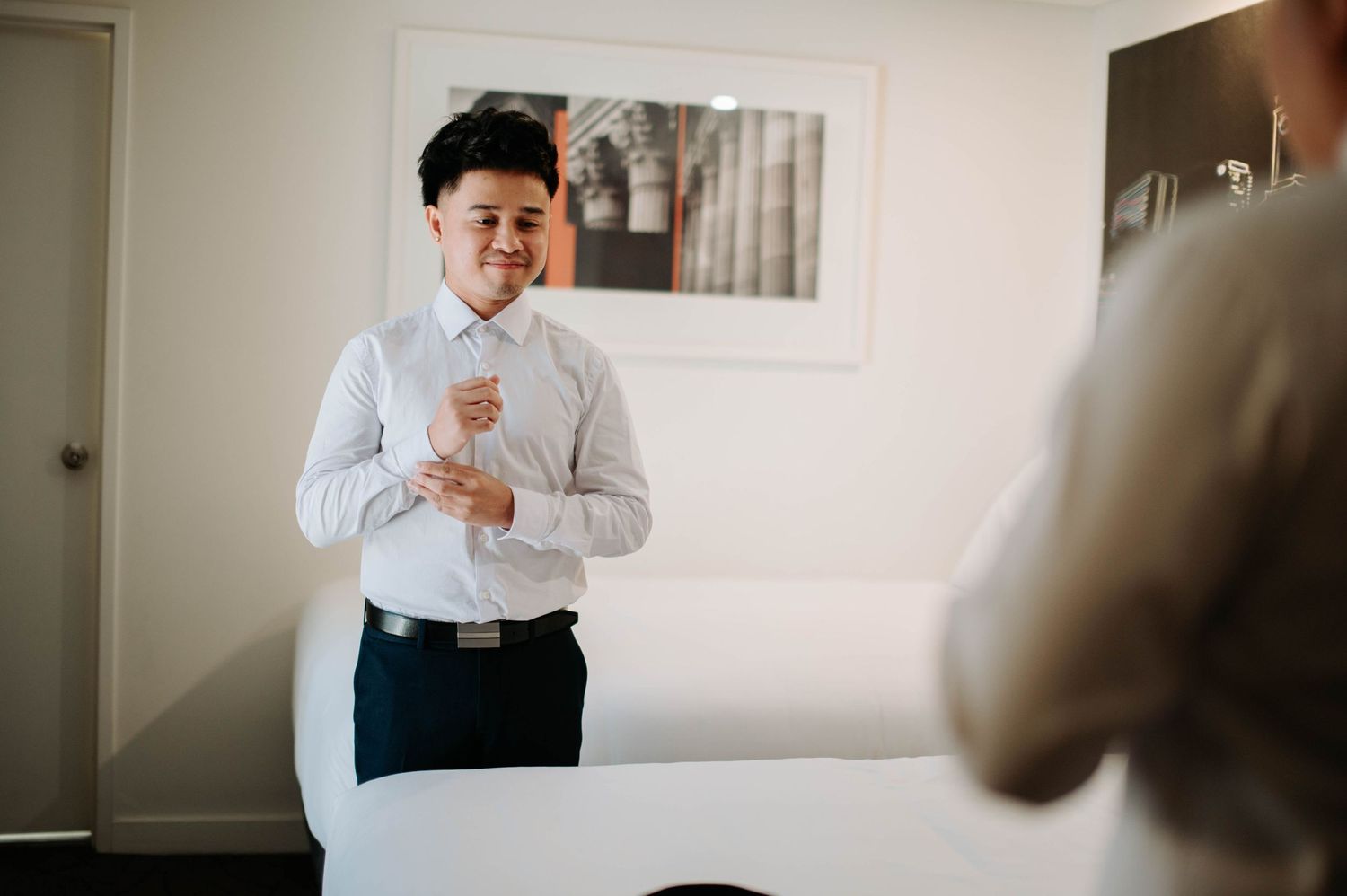A person in a white dress shirt adjusts their cuffs while getting ready in a bright room.