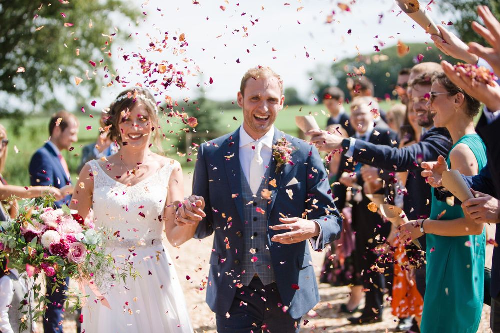 Wedding celebration with confetti being thrown at a couple walking down an aisle during an outdoor ceremony.