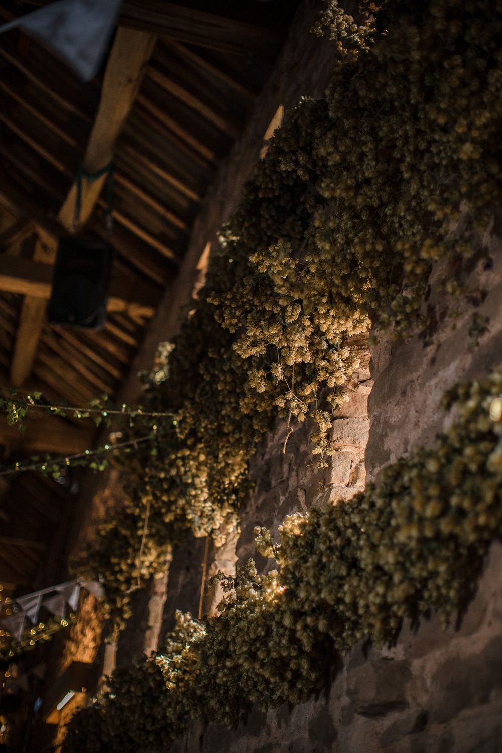 Small white flowers cascade down a stone wall at night under warm lighting and rustic wooden beams.