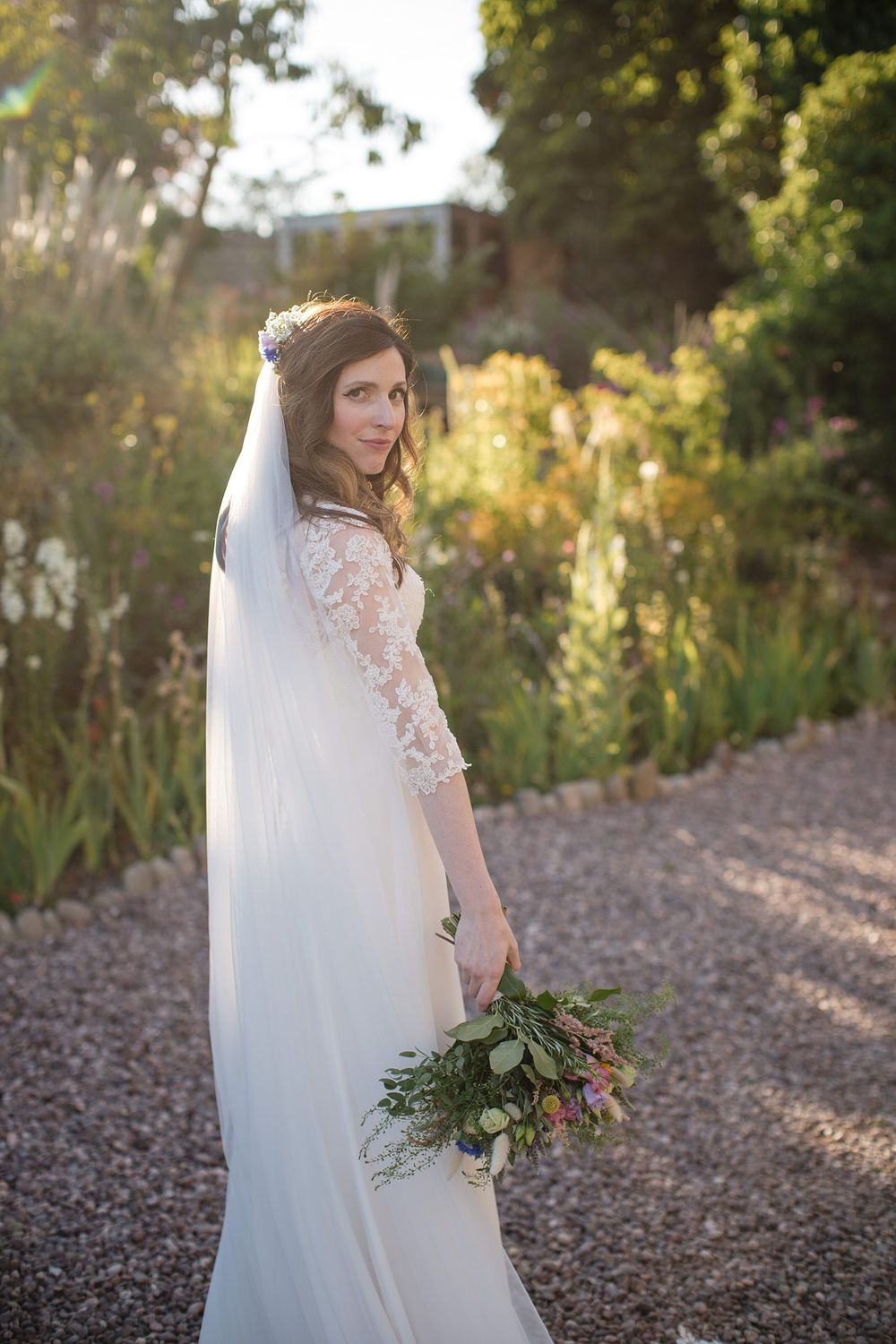 Classic lace wedding gown with flowing veil and natural bouquet in garden setting at golden hour.