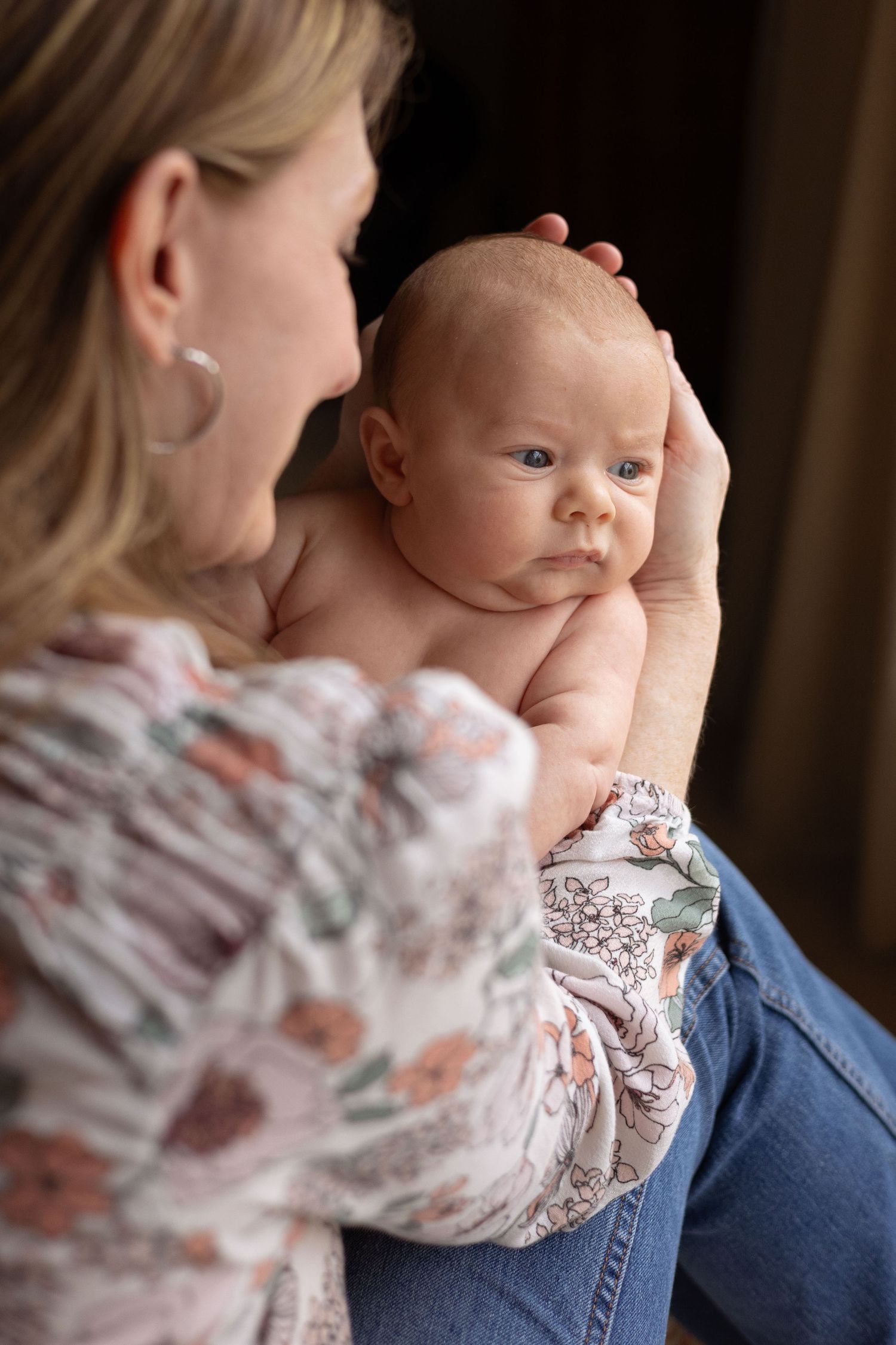 A woman holds her baby as he looks out the window.