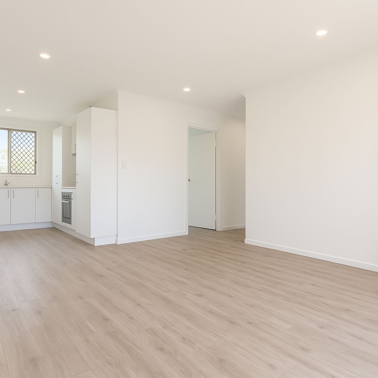 Modern open plan living space with light wood flooring, white walls and recessed lighting in a freshly renovated apartment.
