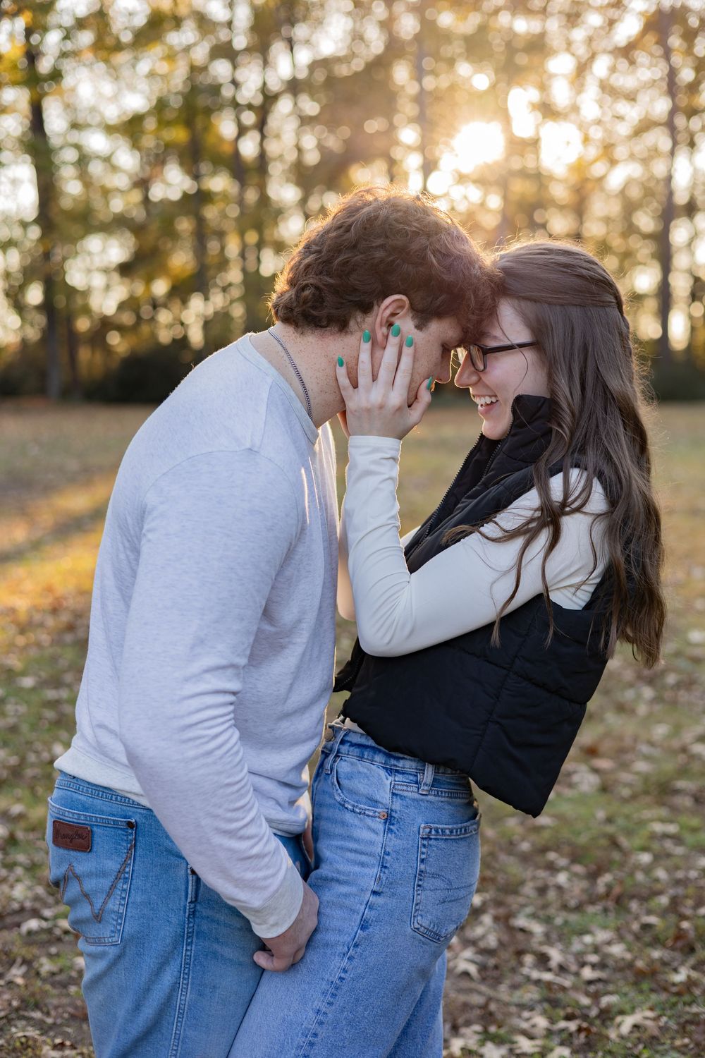 A romantic couple shares intimate moments in a park during golden hour sunset while wearing casual denim and sweaters.
