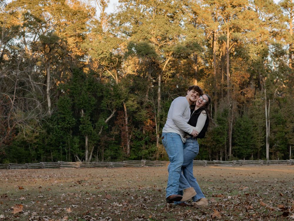 A couple shares a romantic embrace in an autumn forest clearing during golden hour.