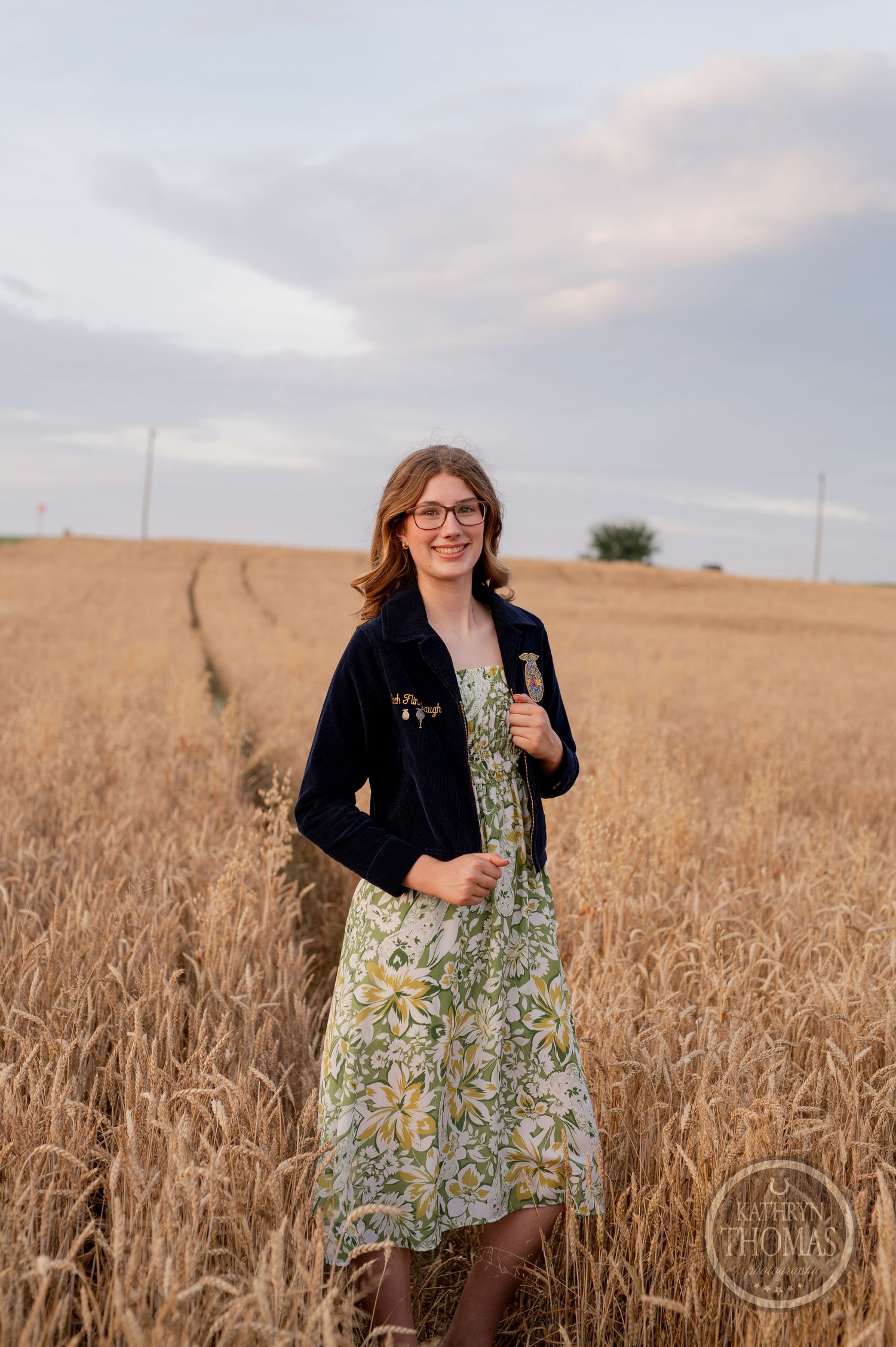 A floral dress and navy cardigan outfit photographed in a golden wheat field at dusk.