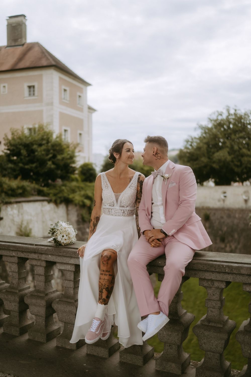 Frau und Mann sitzen auf einem Geländer im Hochzeitsoutfit
