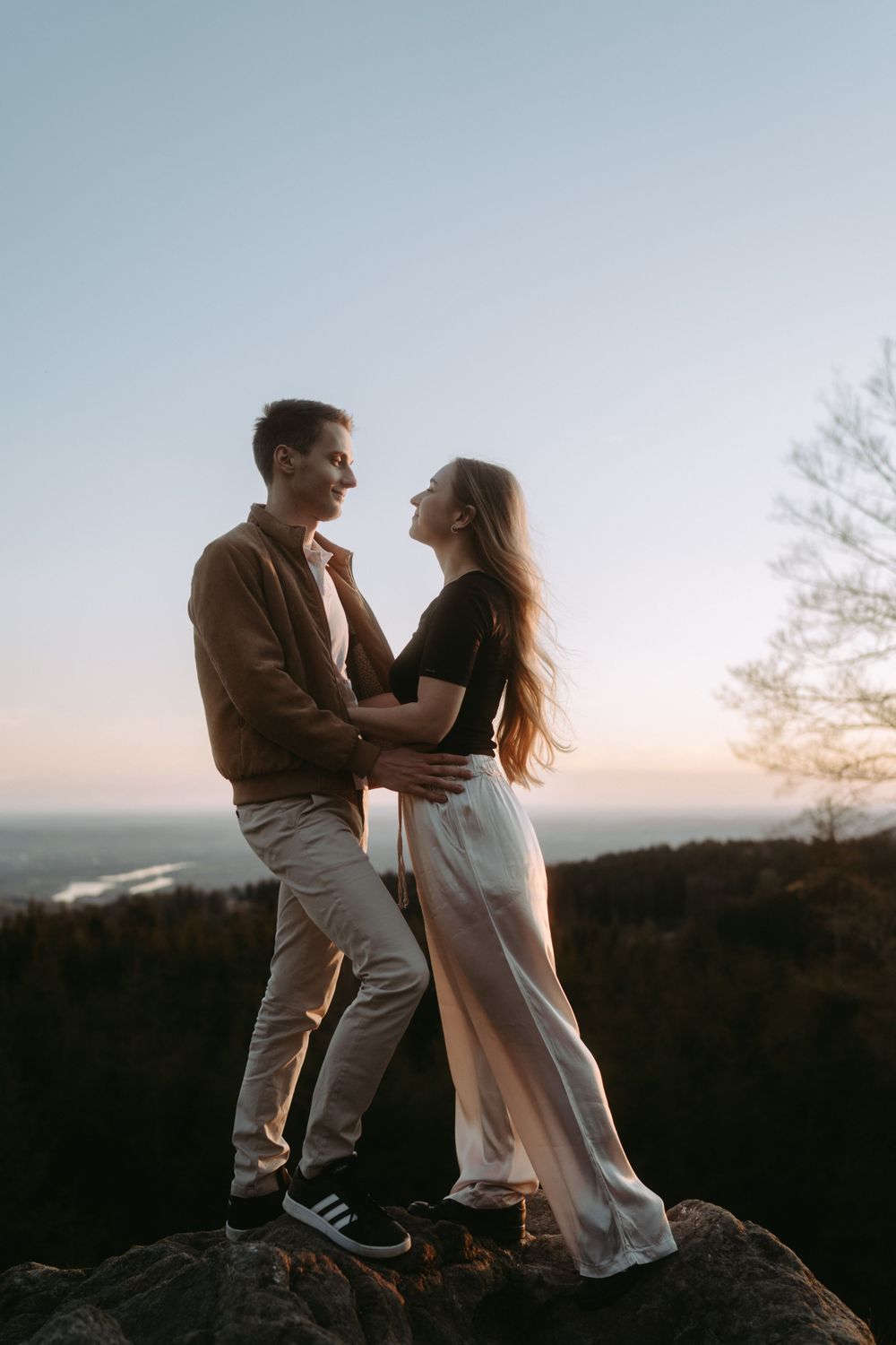 Mann und Frau stehen auf einem Felsen und sehen sich bei Sonnenuntergang in die Augen