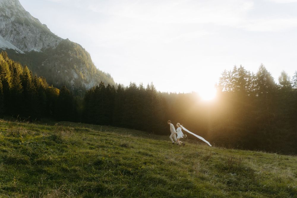 Couple dancing in golden sunset light on alpine meadow with mountain and forest backdrop.