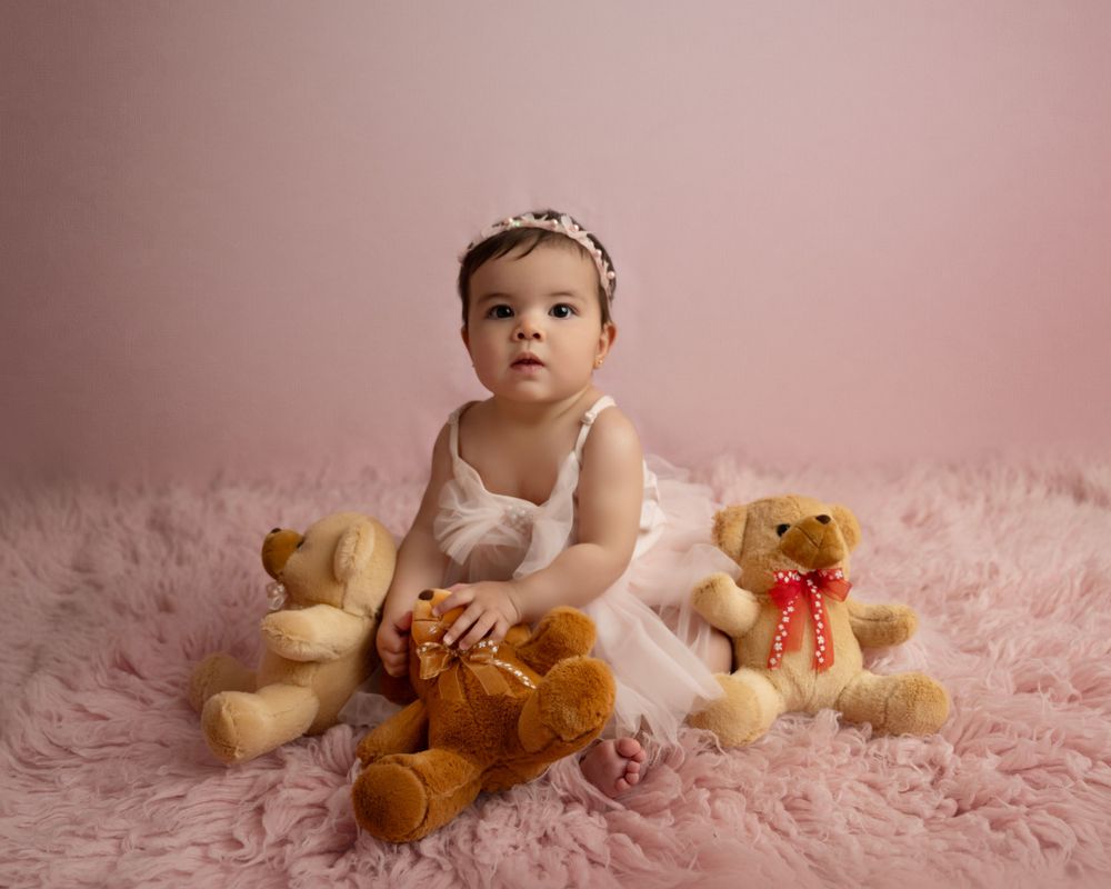 Baby photography session on soft pink backdrop with teddy bears at various ages and poses.