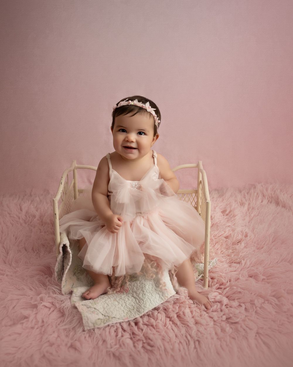 Baby wearing pink tulle dress posing on pink furry backdrop with vintage chair.