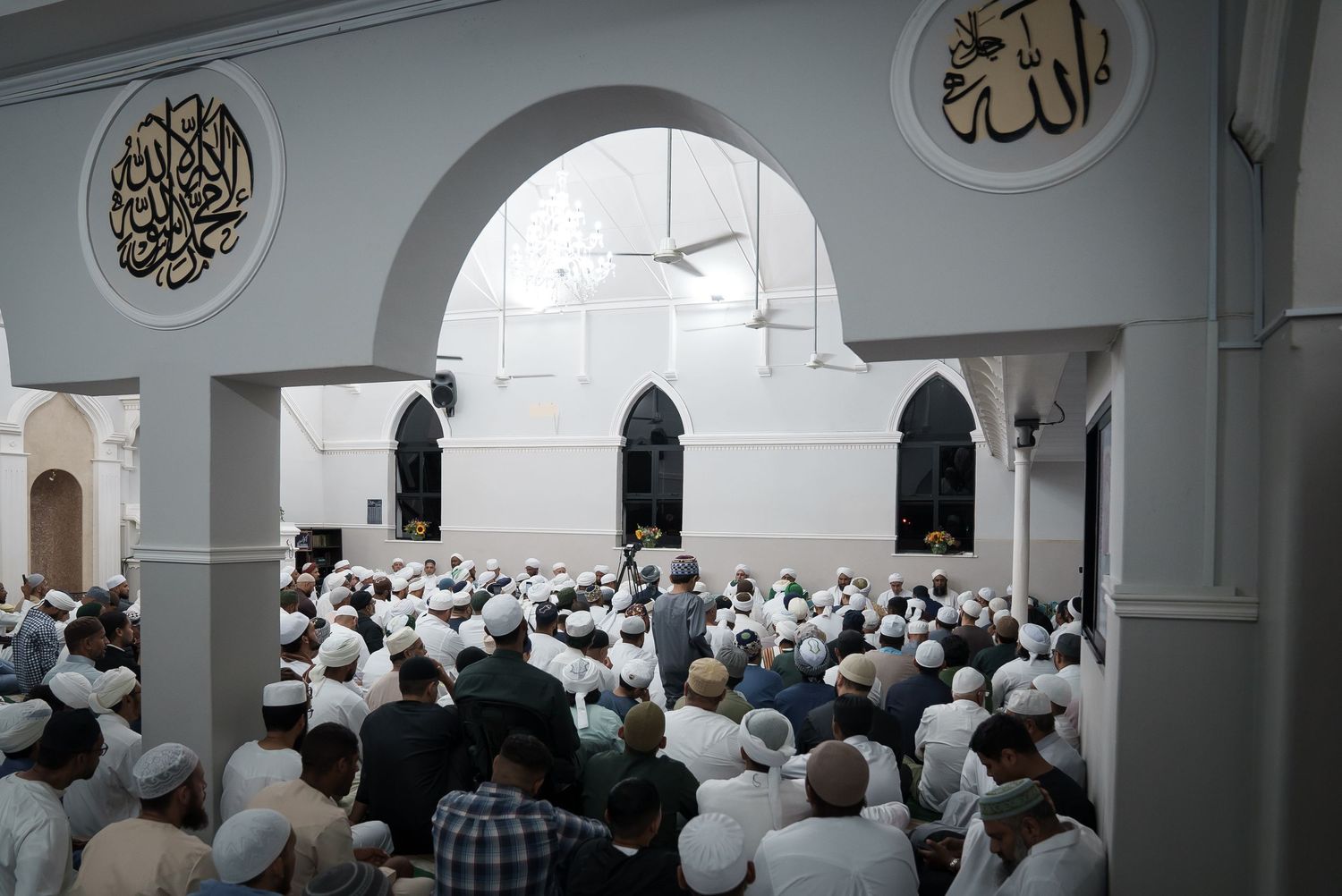 Muslim worshippers gather inside a white-arched mosque during prayer.