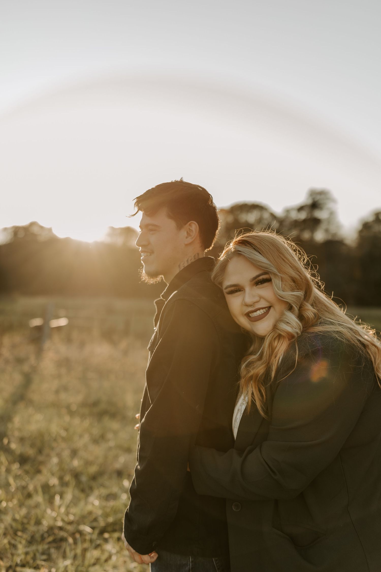 Romantic couple embraces in a sunlit field during golden hour sunset.