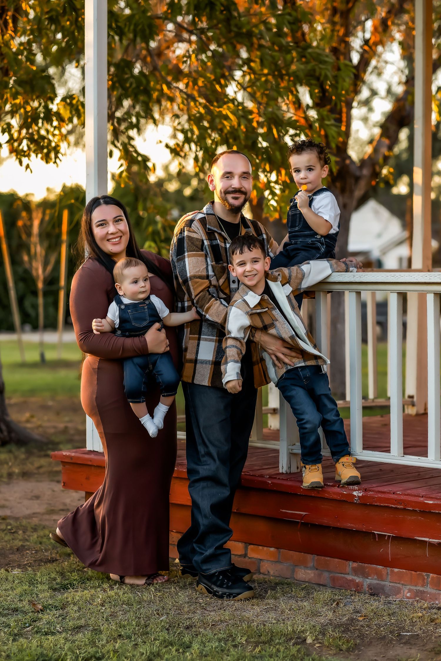 A family standing on wooden porch steps during golden hour amidst autumn trees at Sahuaro Ranch in Glendale Arizona