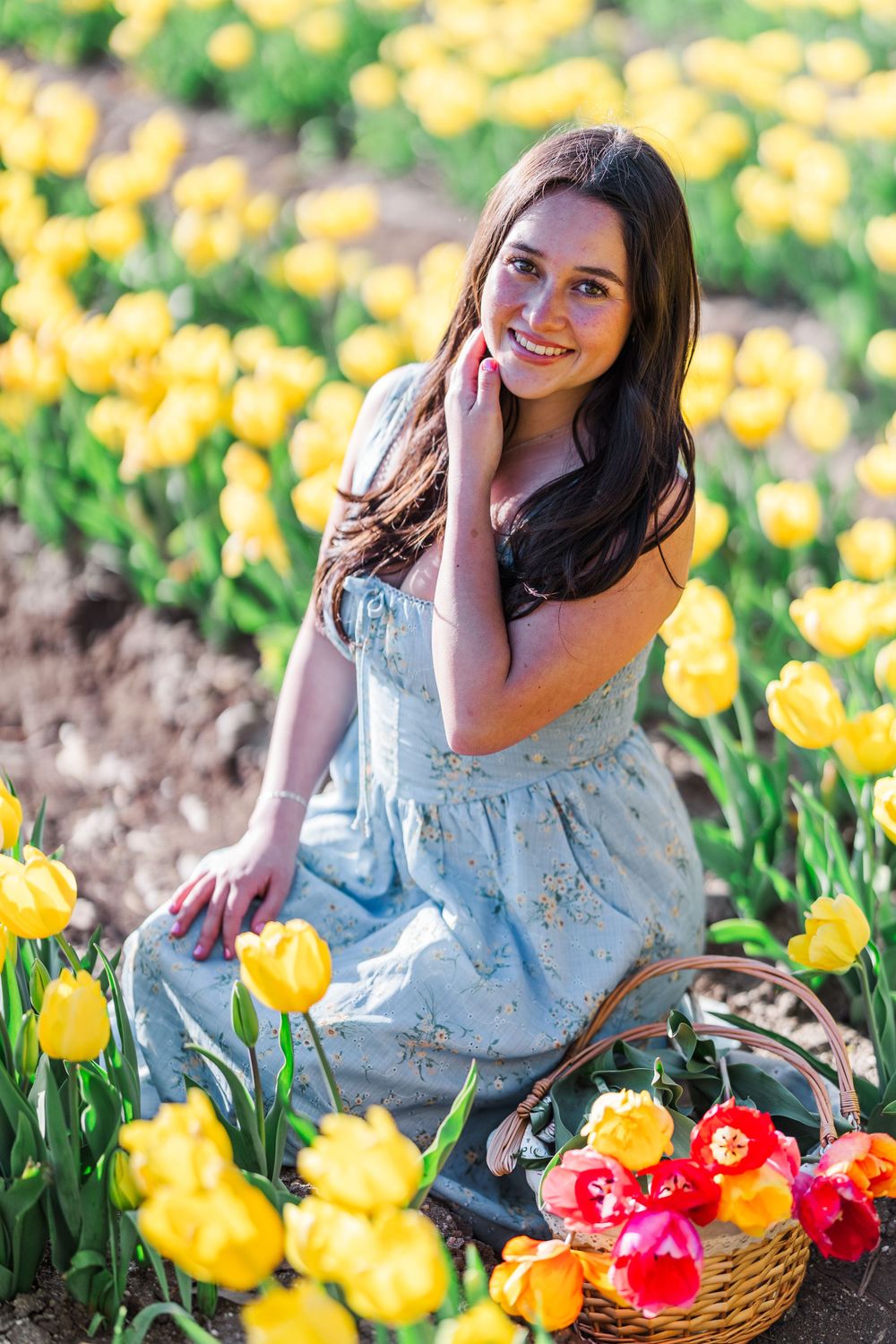 A light blue dress-wearing figure sits among blooming yellow tulips with a flower basket in a spring garden setting.