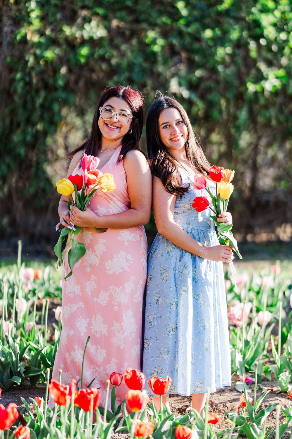 Two friends posing together in floral dresses among colorful tulip flowers.