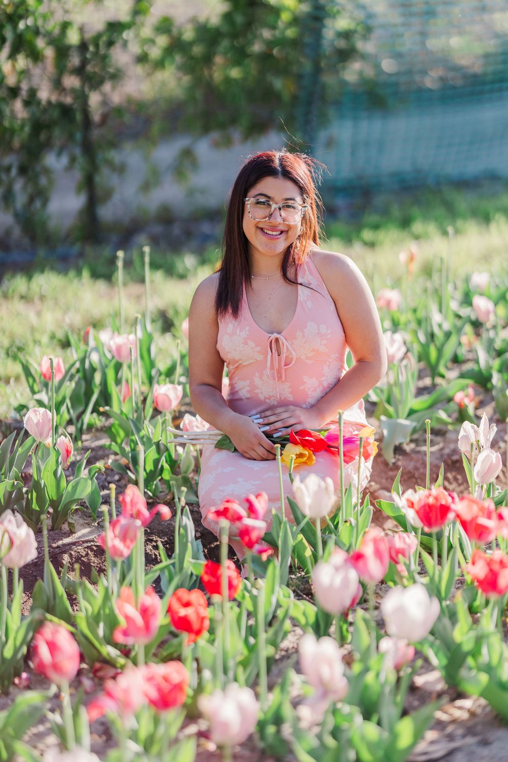 Person in pink dress sitting among pink and red tulips in a garden setting.