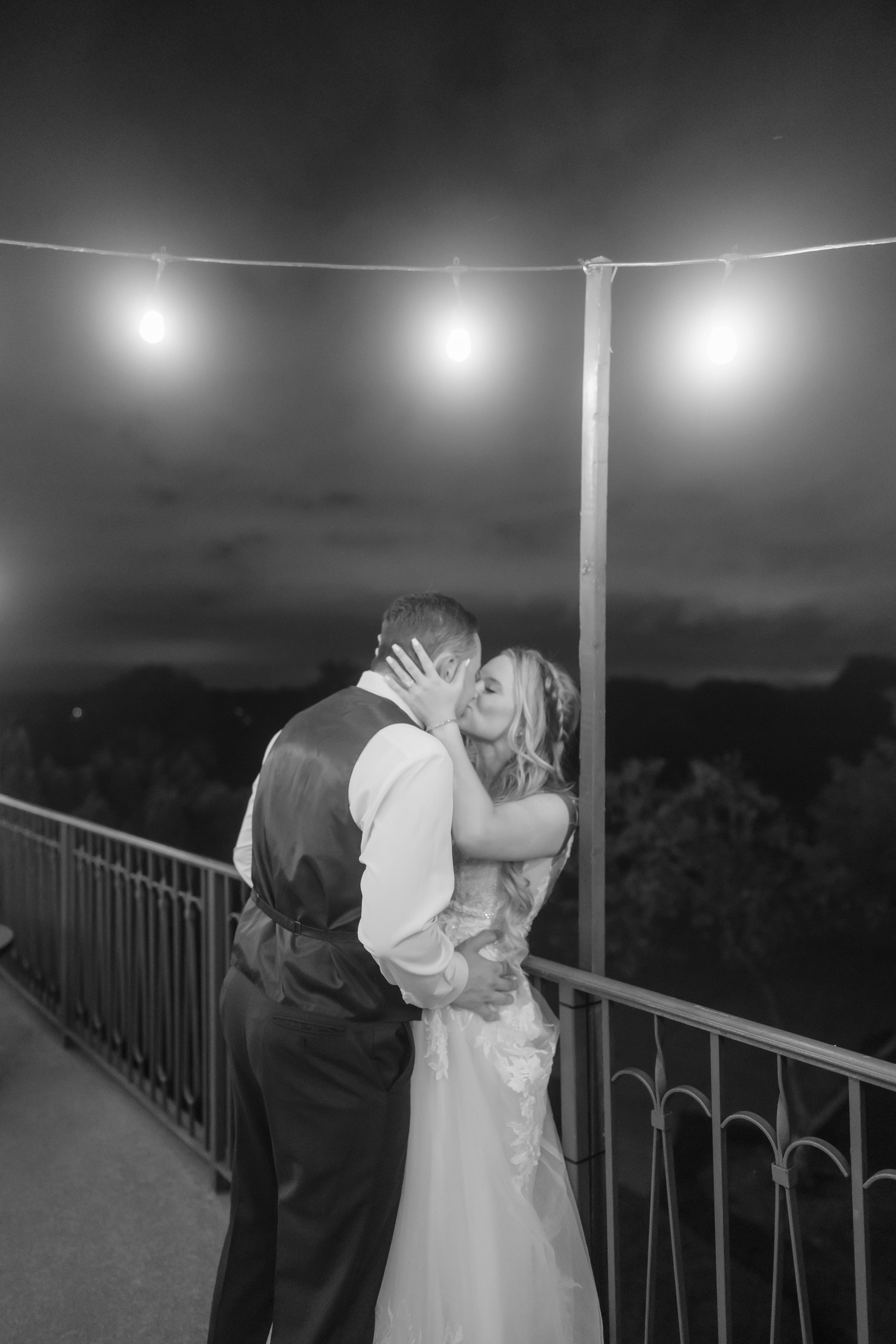 A romantic couple shares a kiss at night on a balcony with string lights glowing overhead in a series of black and white photos.
