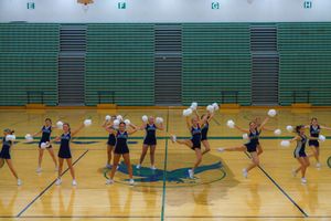 High school volleyball players practicing drills and techniques in a green gymnasium during team practice session.