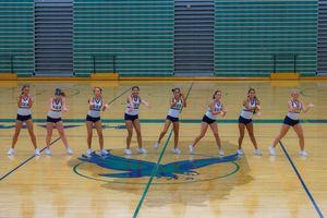High school cheerleaders performing synchronized dance routines in a gymnasium with blue and green court markings.