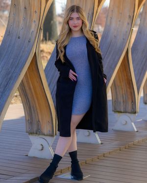 Modern fashion look with black boots, grey dress and black coat on wooden deck.