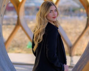 Fashion portrait with black outerwear against geometric wooden architectural elements.