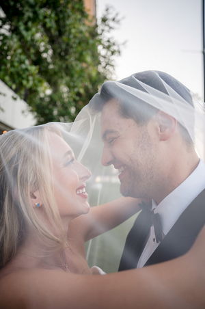 A romantic wedding couple shares an intimate moment under a veil during their outdoor photo session.