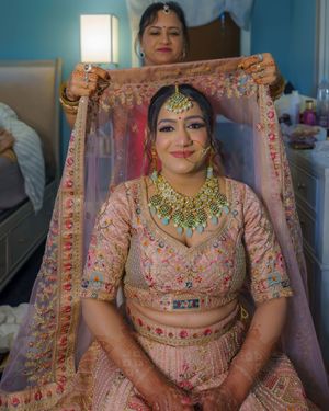 Indian bride wearing ornate pink floral lehenga and traditional gold jewelry set.