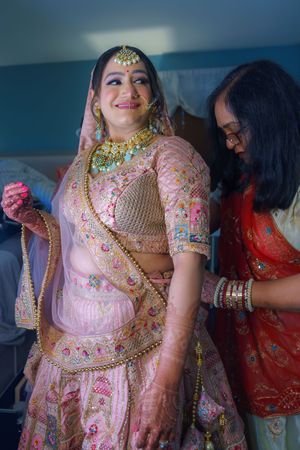 Pink and gold traditional Indian bridal attire being prepared with ornate embellishments and jewelry.
