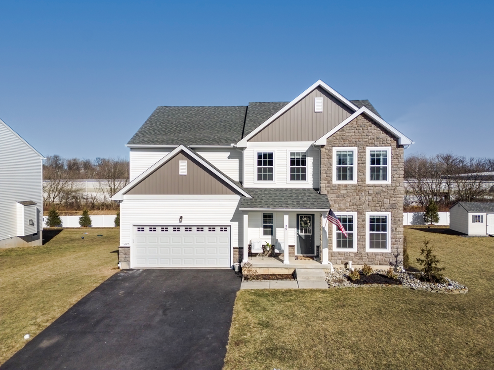 Two-story colonial home with stone facade, white garage, covered porch, and manicured lawn on a sunny day.