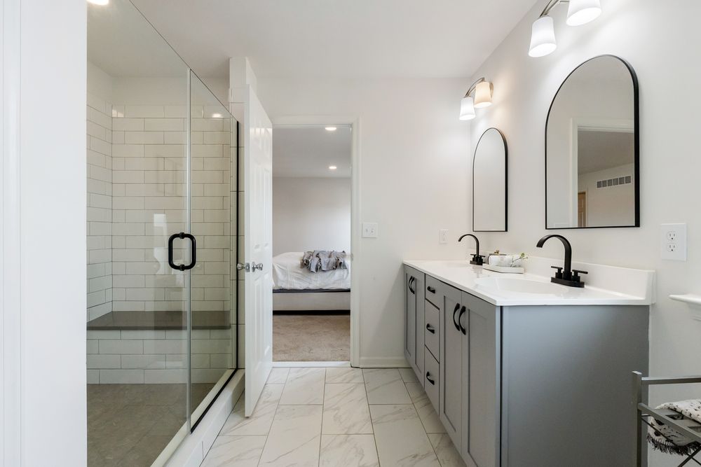 Modern bathroom interior with white subway tile walls, gray vanity cabinet, and arched mirror above sink.