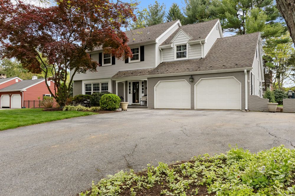 Colonial-style home with double garage, paved driveway, and lush landscaping including a red Japanese maple tree.