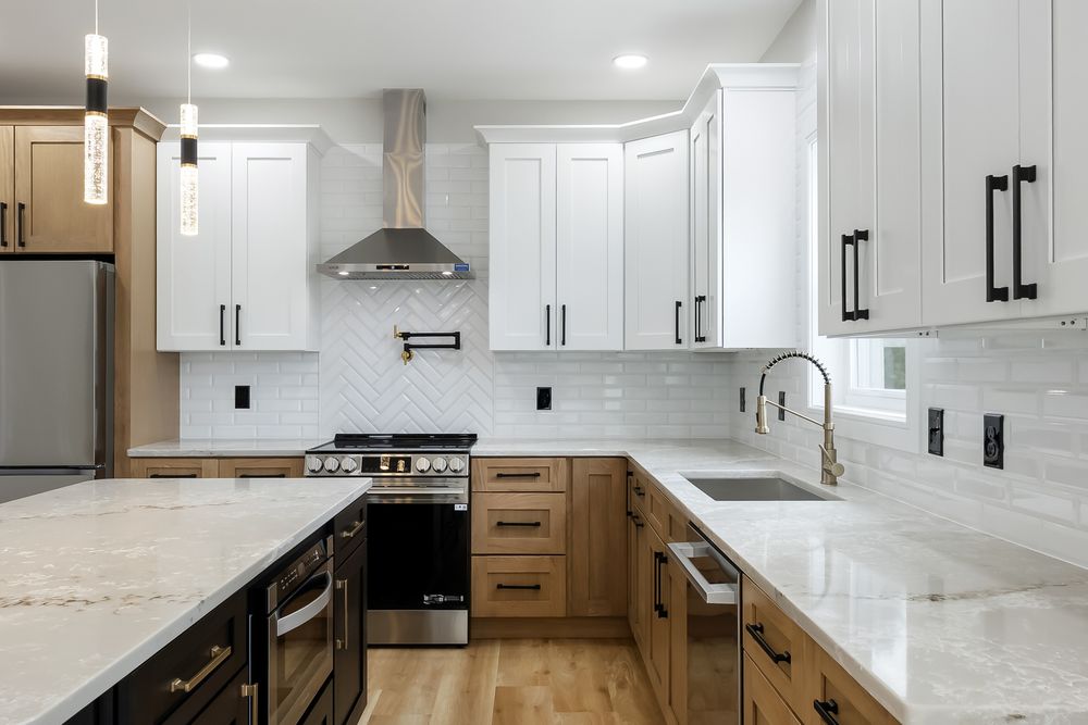 Modern white kitchen with quartz countertops, stainless appliances, and dark hardware against bright white cabinets.