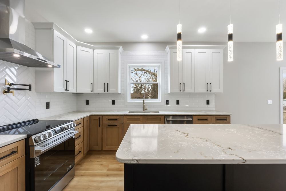 Modern white kitchen with marble countertops, pendant lights, and wood accents showcases a clean transitional design.