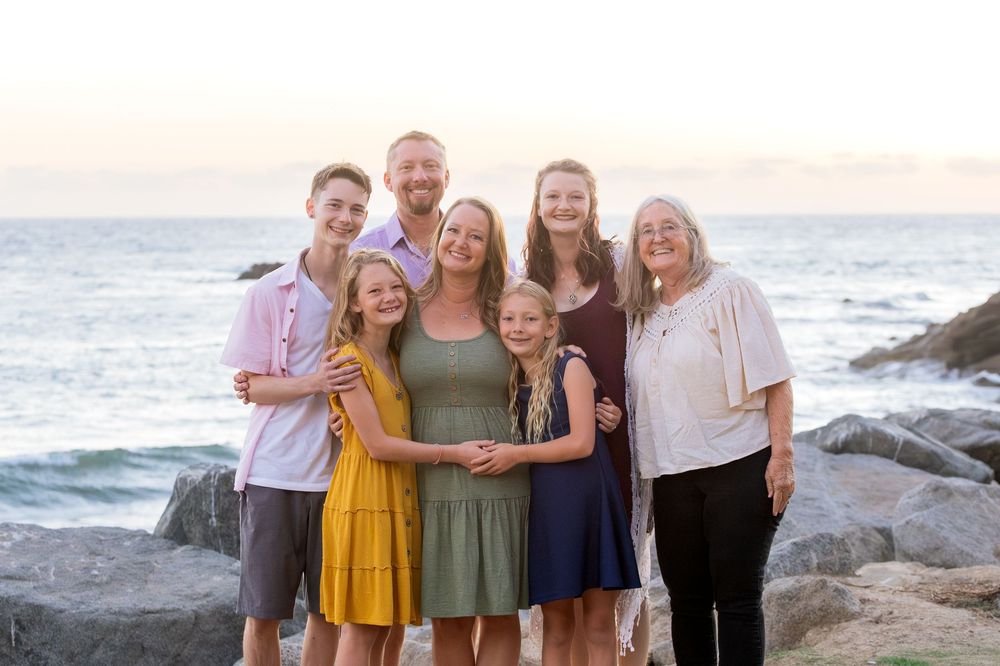 A group of people pose together on a rocky beach at sunset with ocean waves in the background.