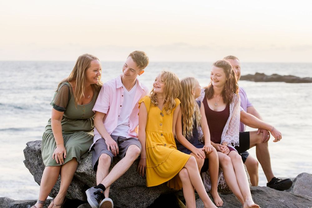 A group of friends sit together on a beach at sunset sharing laughter and conversation.