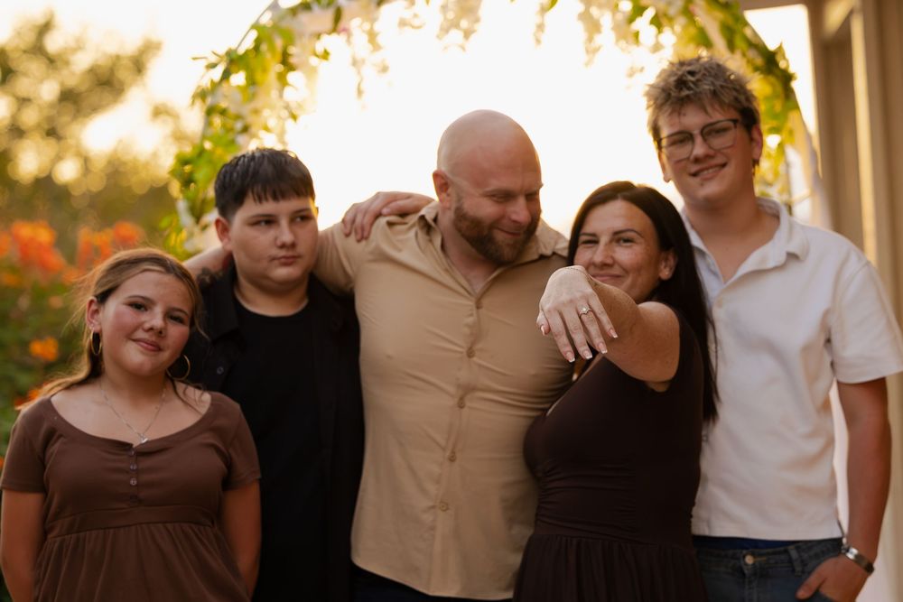 Family of five smiling together outdoors at golden hour, posing for a group portrait in warm evening light.